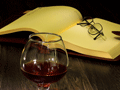 detail wine glass on table with pair of eyeglasses on open book pages 