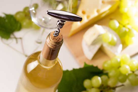 Corkscrew in cork of wine bottle; cheese platter and grapes in background